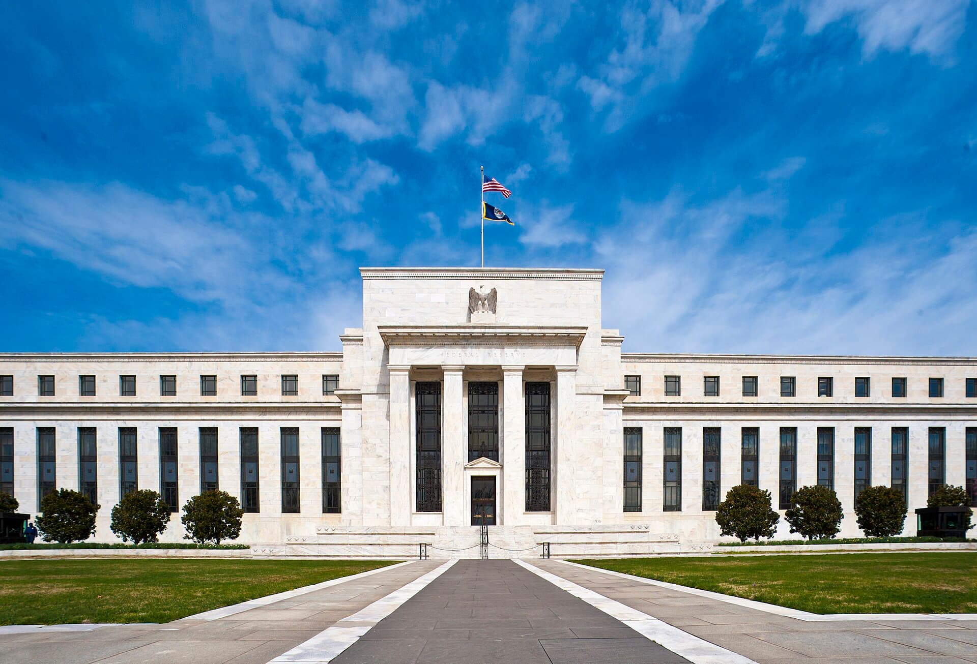 The white marble facade of the Marriner S. Eccles Federal Reserve Board Building in Washington, D.C., with flags flying above