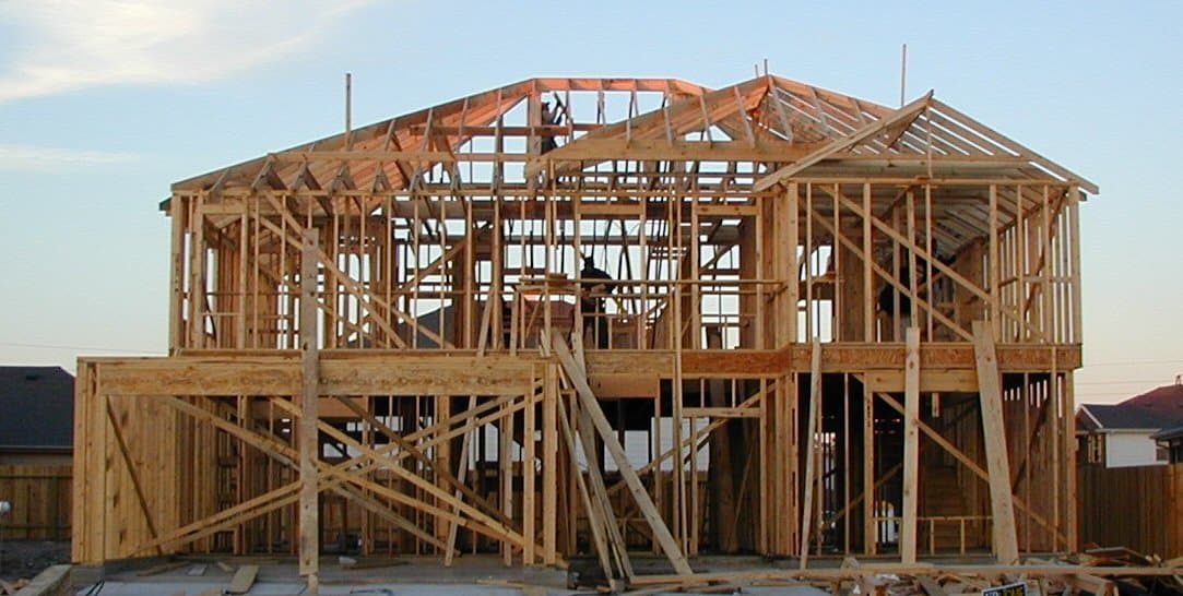 The exposed wood framing of a two-story house under construction against a pale evening sky