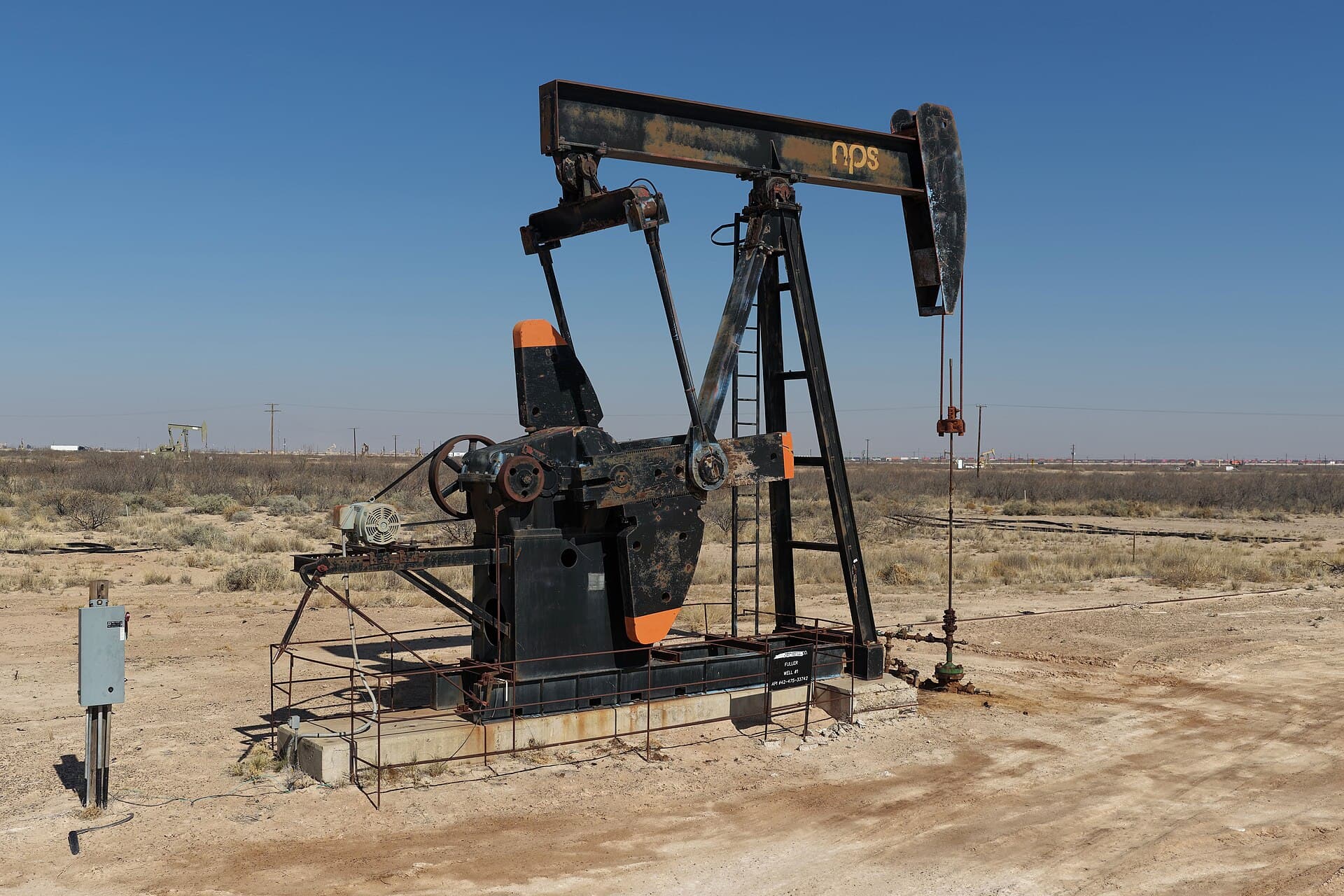 A black oil pumpjack standing in a flat desert oil field under a clear blue sky