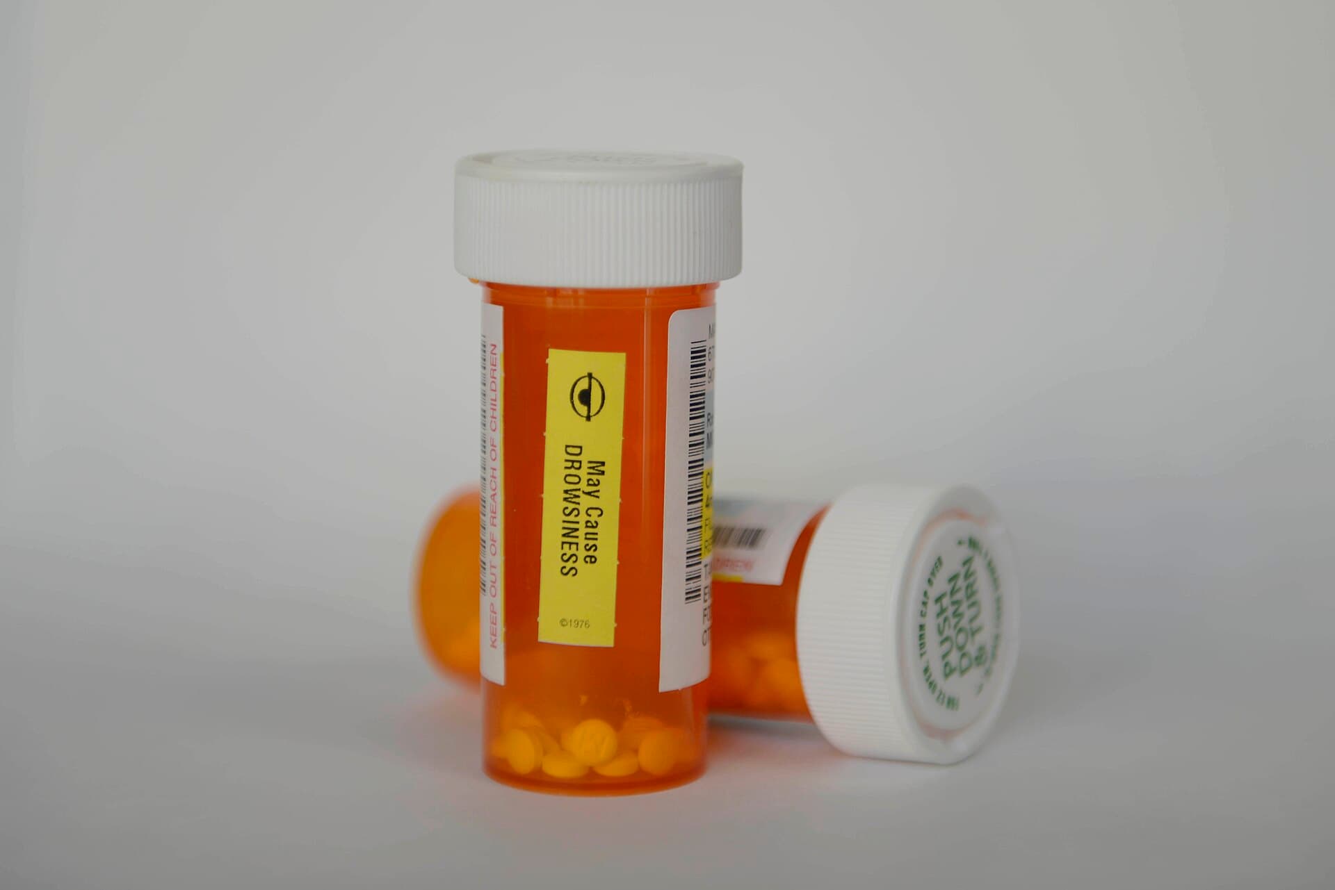 Two amber prescription pill bottles with white caps, one upright and one on its side, on a plain light background